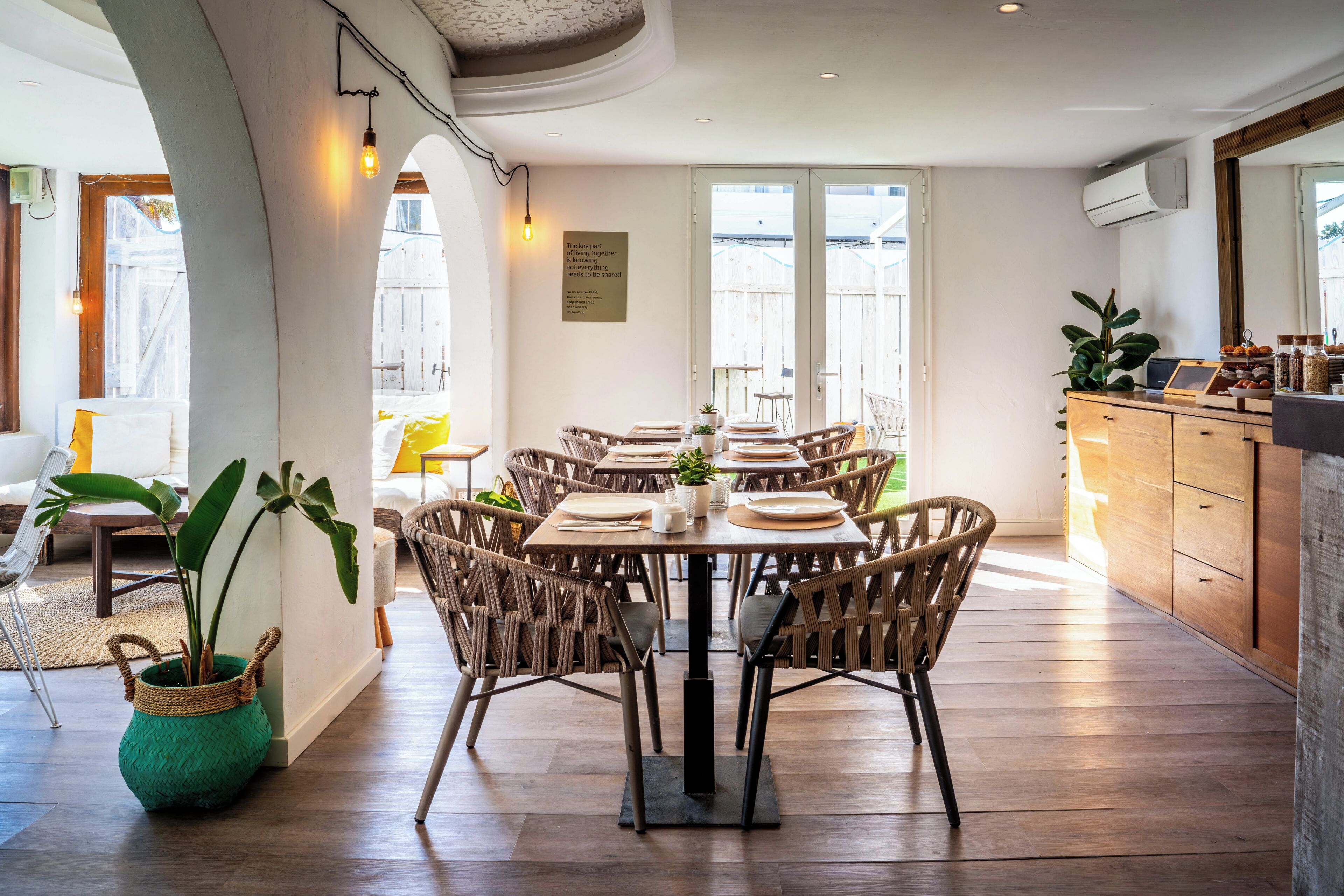 Un comedor con una mesa redonda, sillas de mimbre y una planta verde en una maceta tejida.