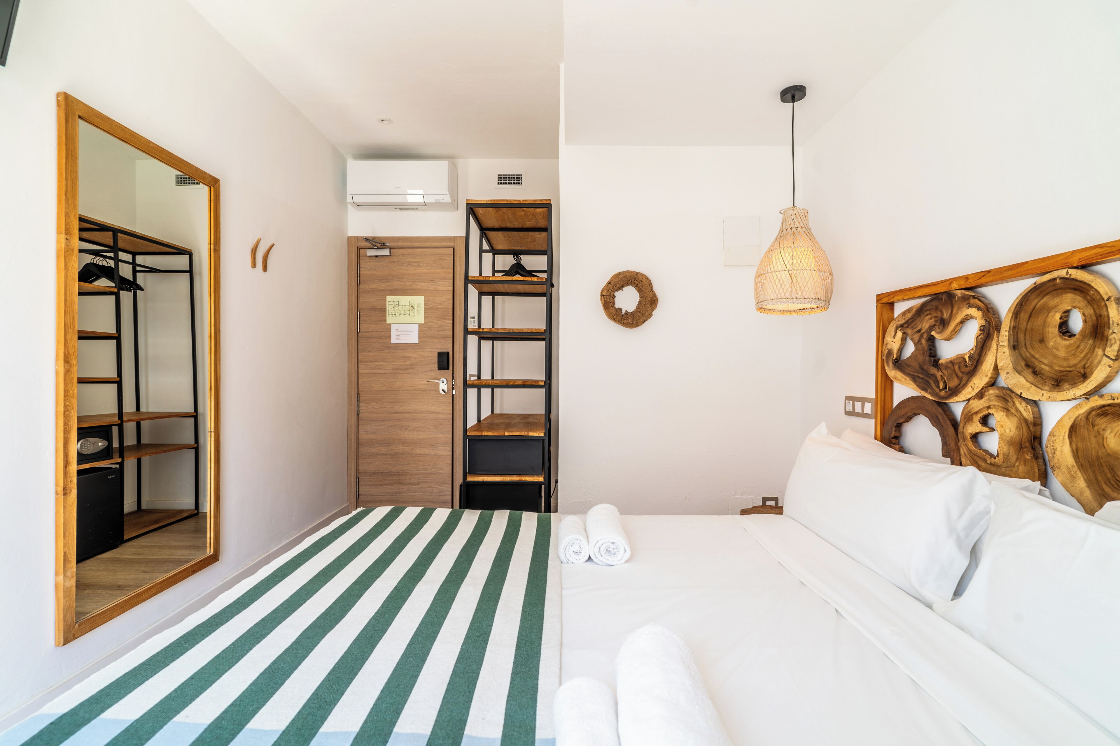 Una habitación con un armario espejado, una cama con colcha a rayas, una estantería de madera y una obra de arte de madera colocada en la pared.