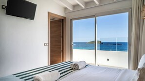 A hotel room with a bed, a TV, a sliding glass door to the sea, and a wooden door. - Outsite Ibiza - Work, Connect, Explore (Santa Eulalia del Rio)