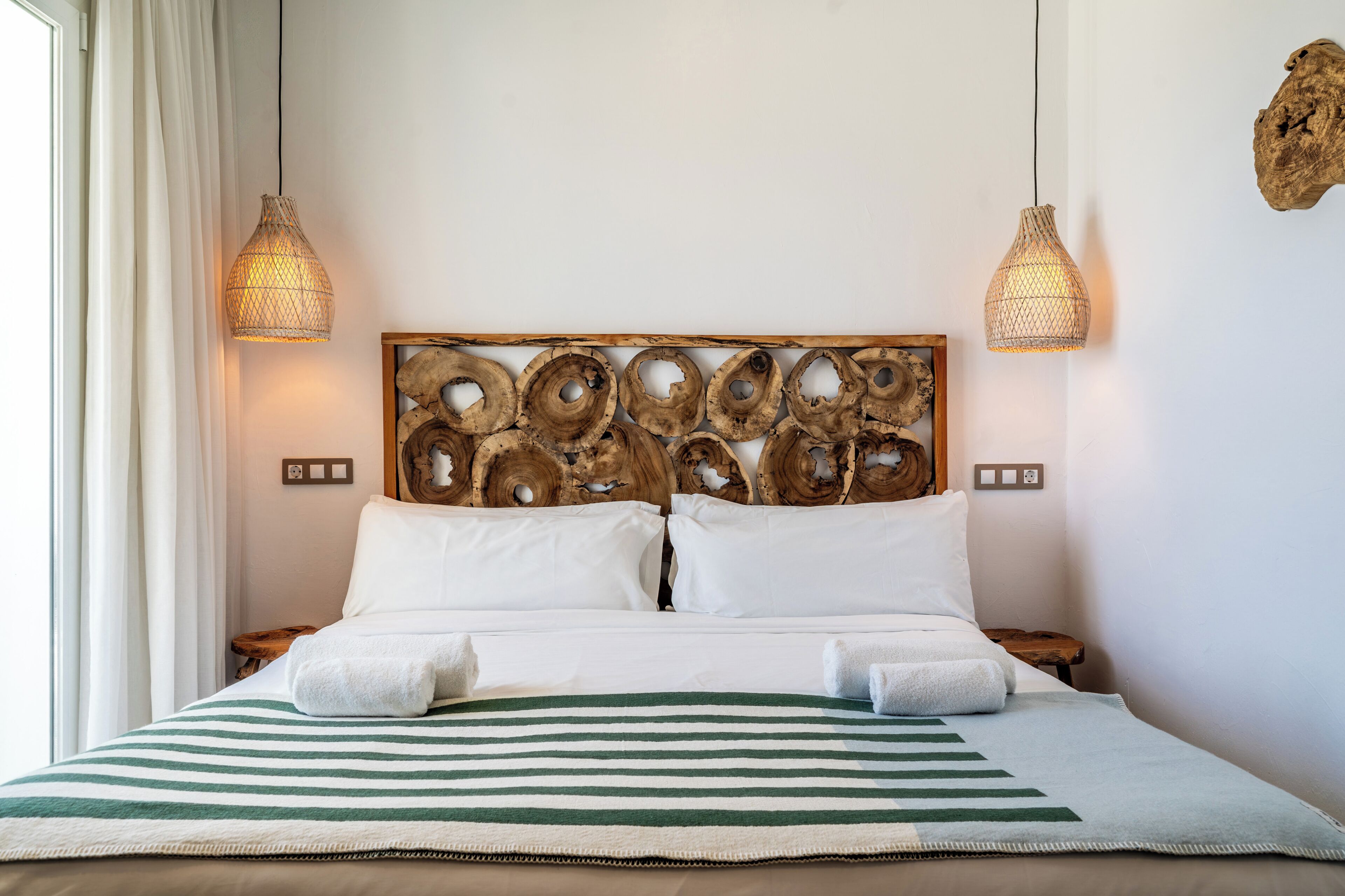 A neatly made bed with a striped bedspread, two bedside lamps, and a unique wooden headboard.