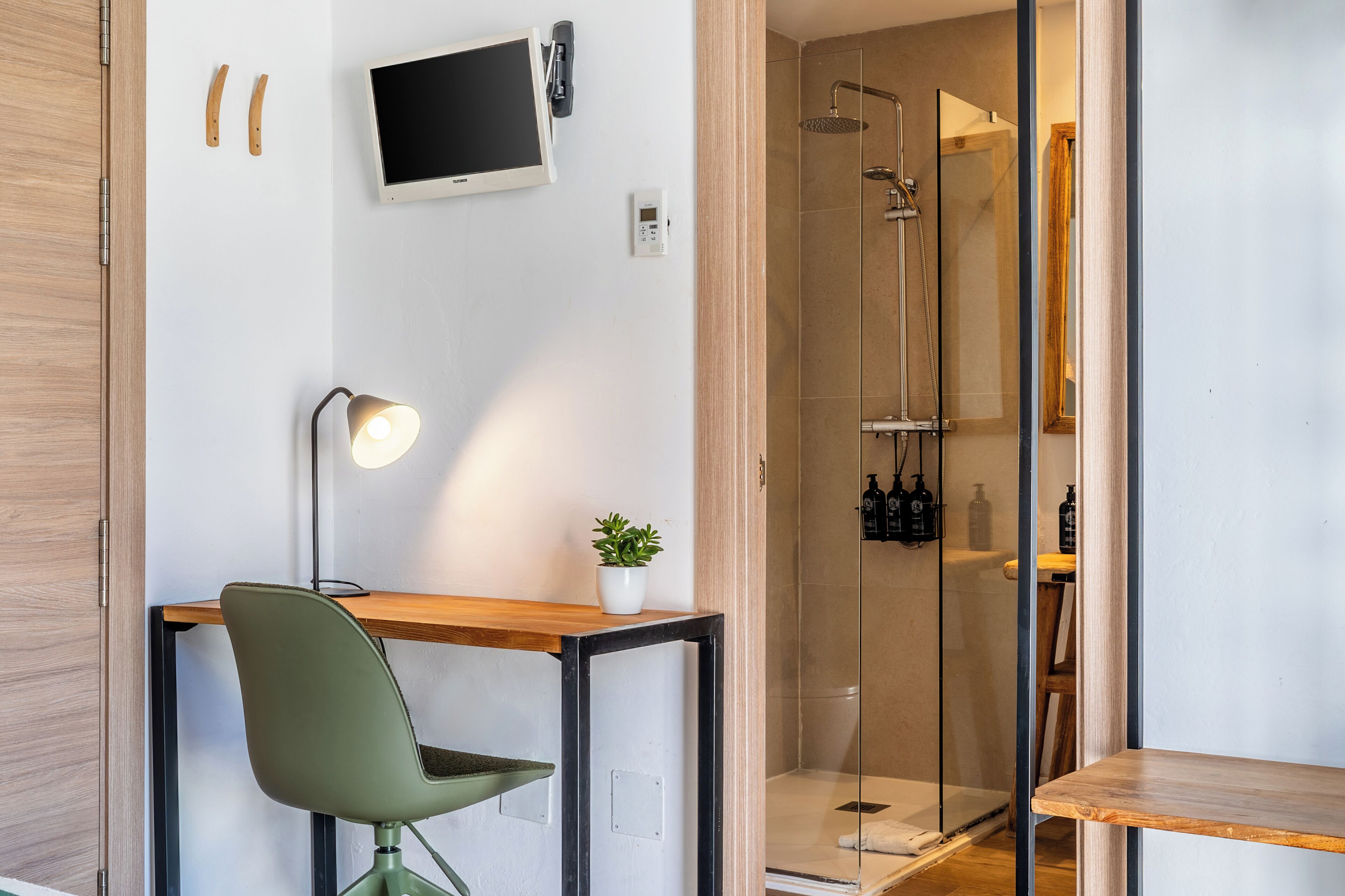 A modern bathroom with a shower, a mounted TV, and a desk with a chair.