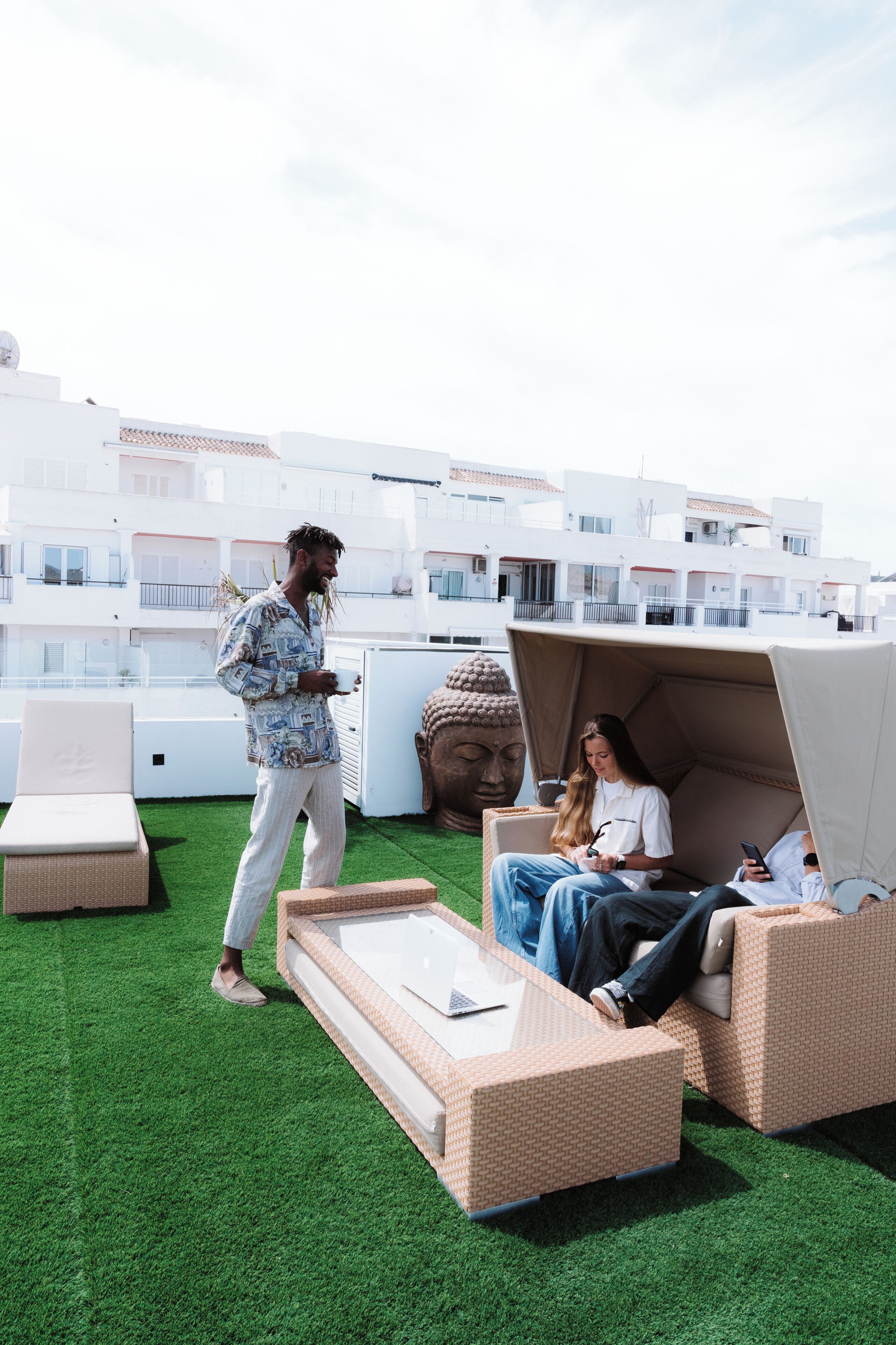 A rooftop terrace with artificial grass, wicker furniture, and a Buddha statue.