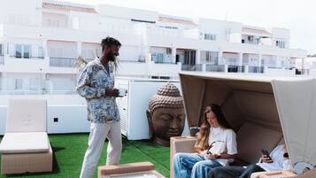 A rooftop terrace with artificial grass, wicker furniture, and a Buddha statue.