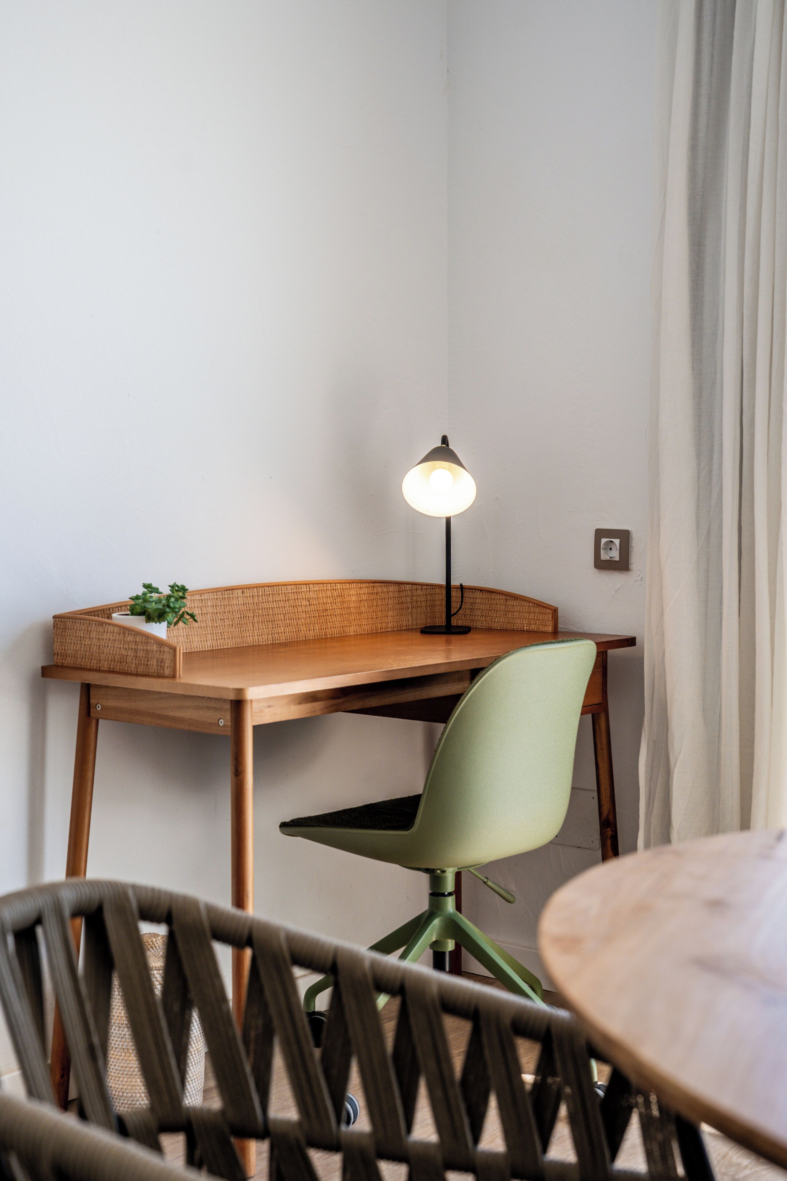 A room with a wooden desk, a green chair, a small table, and a floor lamp.