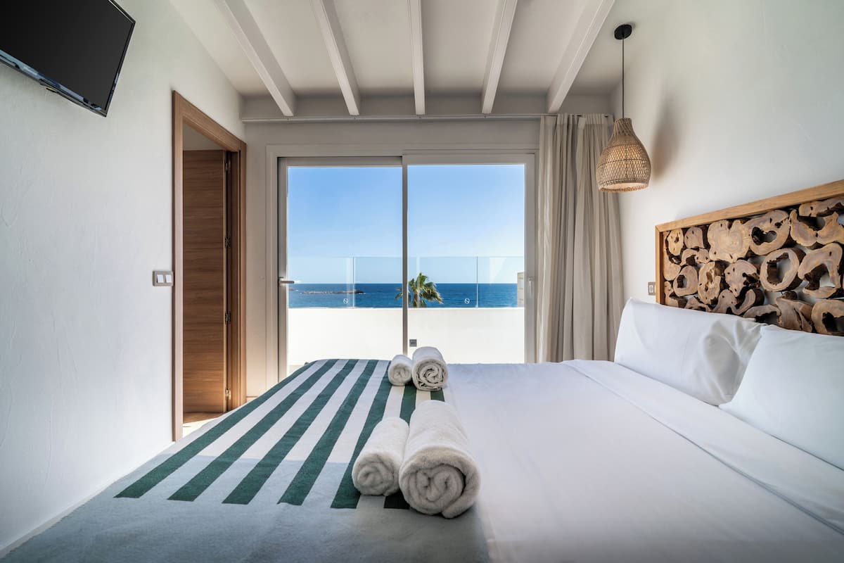 Habitación de hotel con cama, vista al mar, televisión en la pared y cabecero de madera.