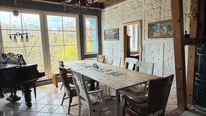 Comedor con una larga mesa, sillas, un piano y vistas a través de amplios ventanales.