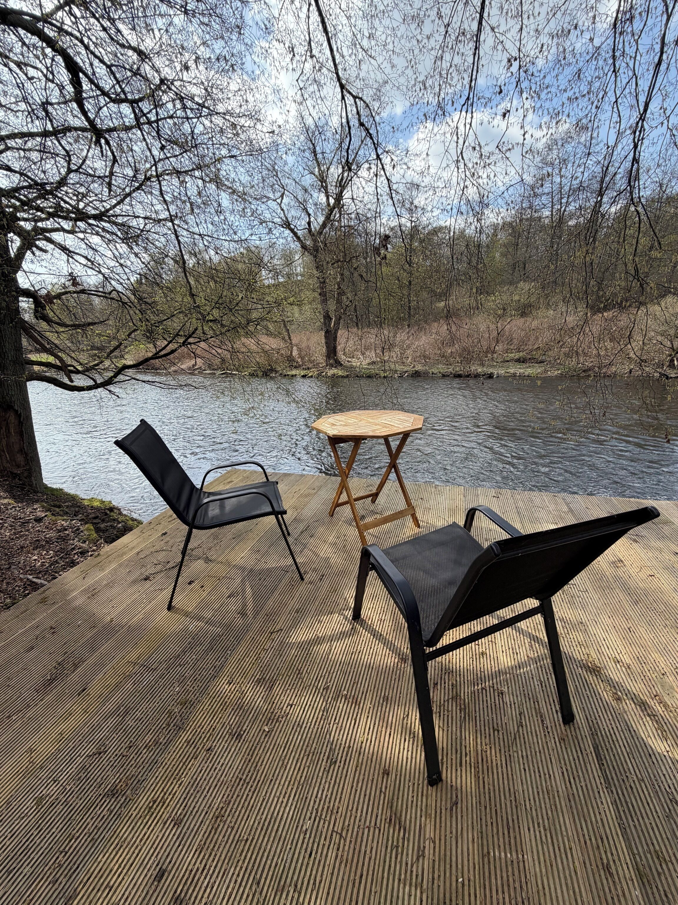 A wooden deck with a table and two chairs overlooking a river.
