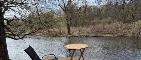 A wooden deck with a table and two chairs overlooking a river.