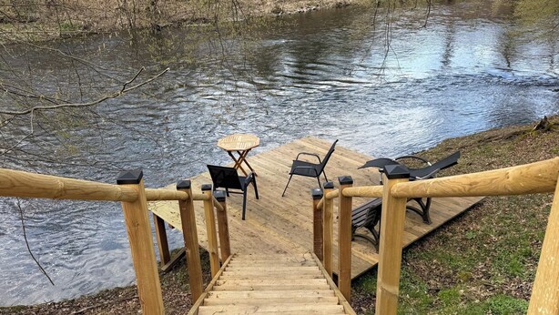 Una escalera de madera que lleva a un muelle con sillas y una mesa junto a un río.