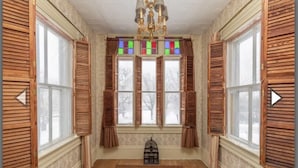 A room with wooden shutters, a chandelier, and a birdcage on the floor. - Heart of Pubnico (Pubnico)