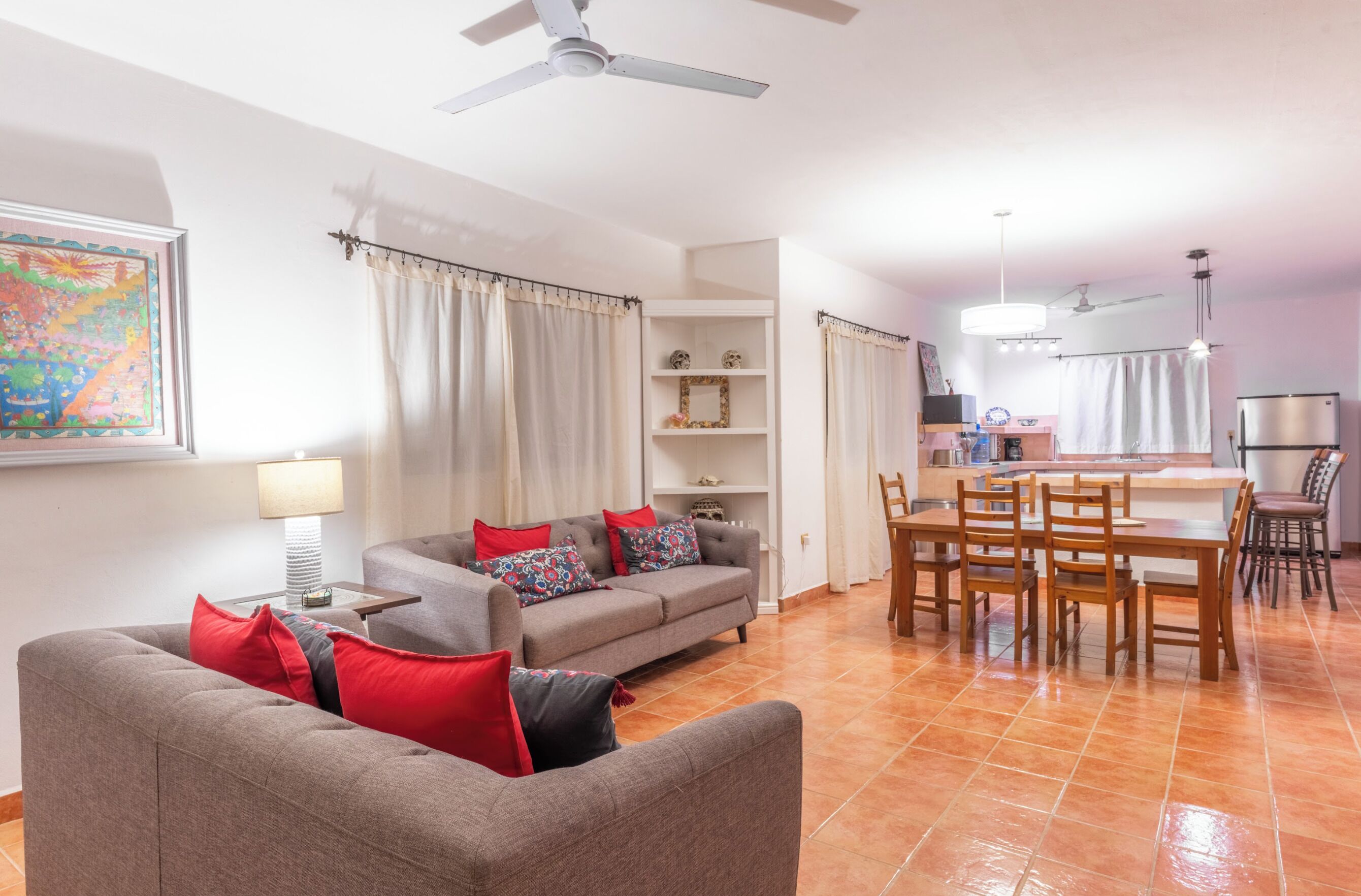 Un salon avec un canapé, une table à manger avec des chaises, un ventilateur de plafond et un coin cuisine équipé d’un réfrigérateur.