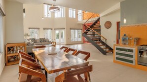 Amplia sala de estar con una mesa de comedor de madera, un sofá y una escalera que lleva a un nivel superior.
