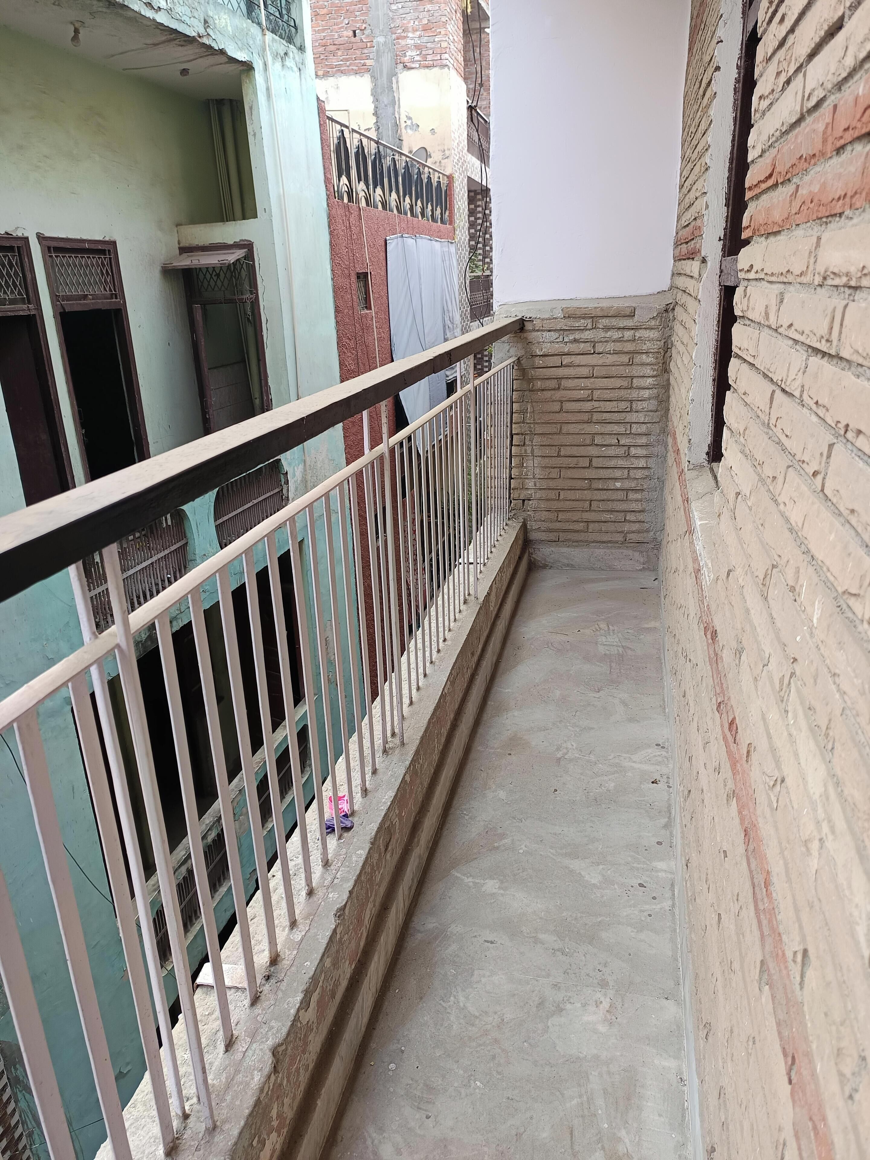 Un couloir étroit avec une rambarde métallique, un sol en béton et des murs en briques.