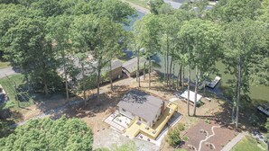 An aerial view of a residential area with a large house surrounded by trees, a dock extending into a lake, and a clear sky. - Charming Lake Front Home - Pet Friendly (Lake Norman of Catawba)