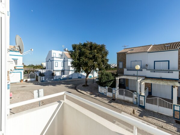 A residential area with white buildings, a large tree, and a clear blue sky.
