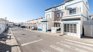 A street view with a row of white buildings with blue trim and a clear blue sky.
