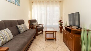 A living room with a sofa, armchair, coffee table, TV stand, and a painting on the wall.