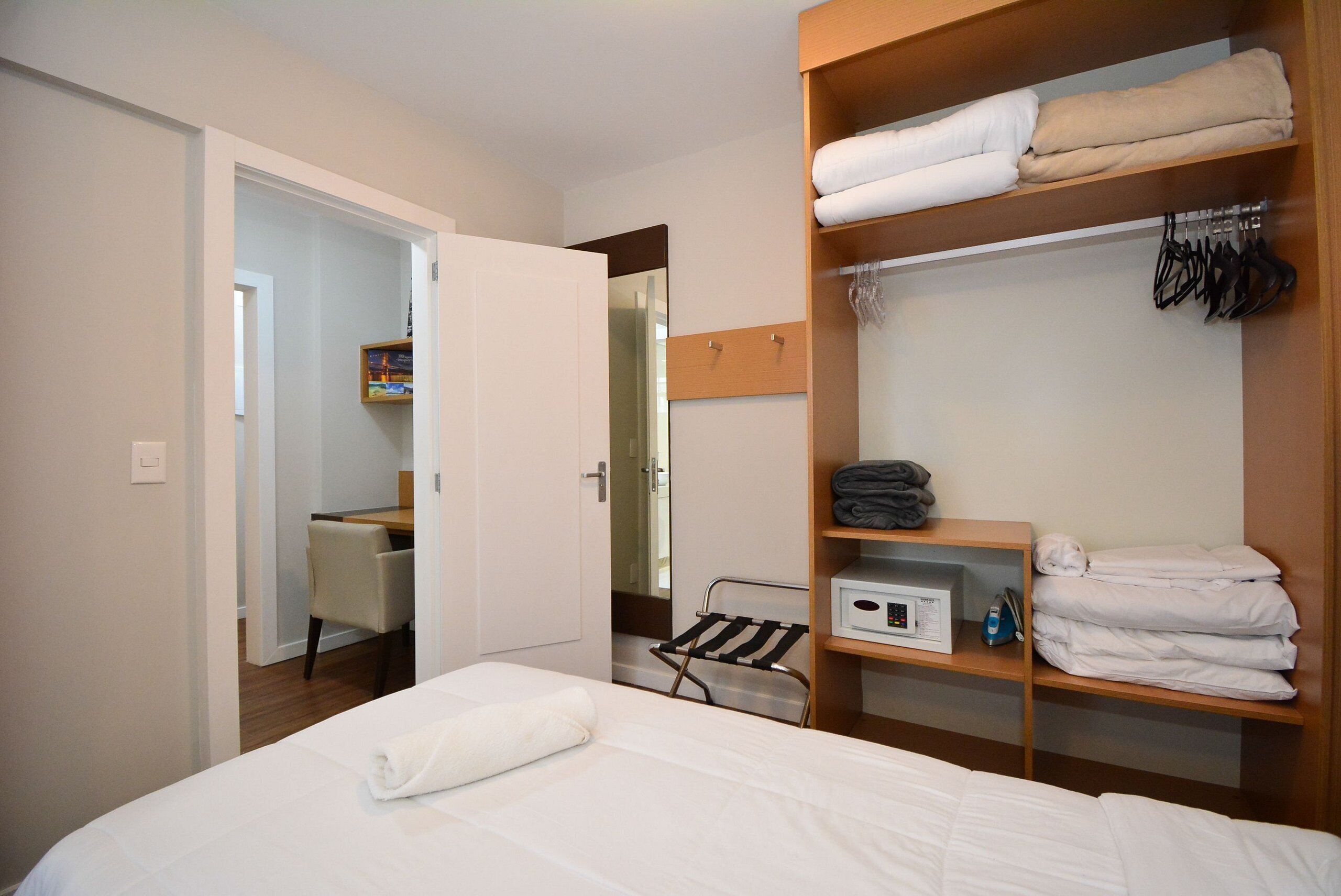 Una habitación de hotel con cama, un armario de madera con toallas dobladas, una mesita y una silla.