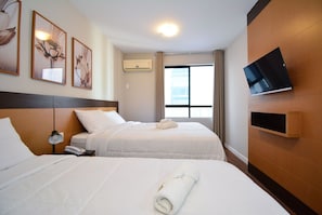 Habitación de hotel con dos camas, un televisor en la pared y una ventana con cortinas.