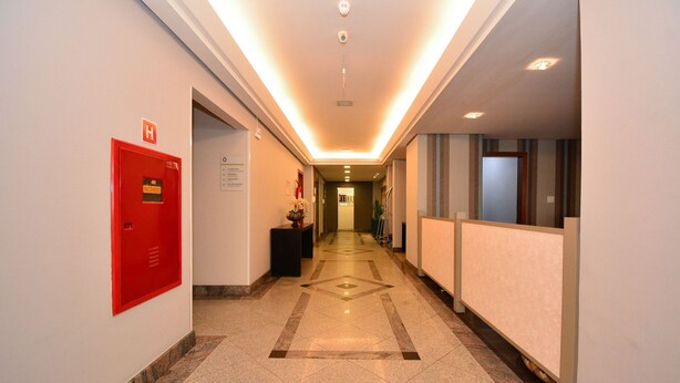 A hotel hallway with a red emergency exit sign, a reception desk, and a patterned floor.