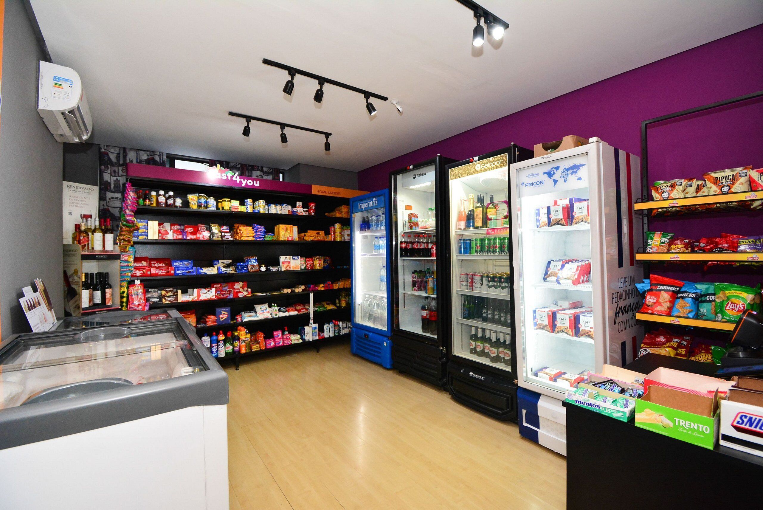 A store with shelves stocked with various snacks and beverages, a freezer, and a display case with boxed products.