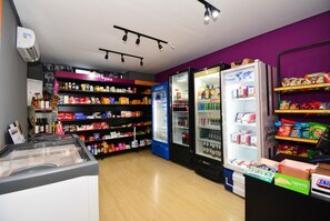 Una tienda con estantes llenos de diferentes aperitivos y bebidas, un congelador y un expositor con productos en caja.