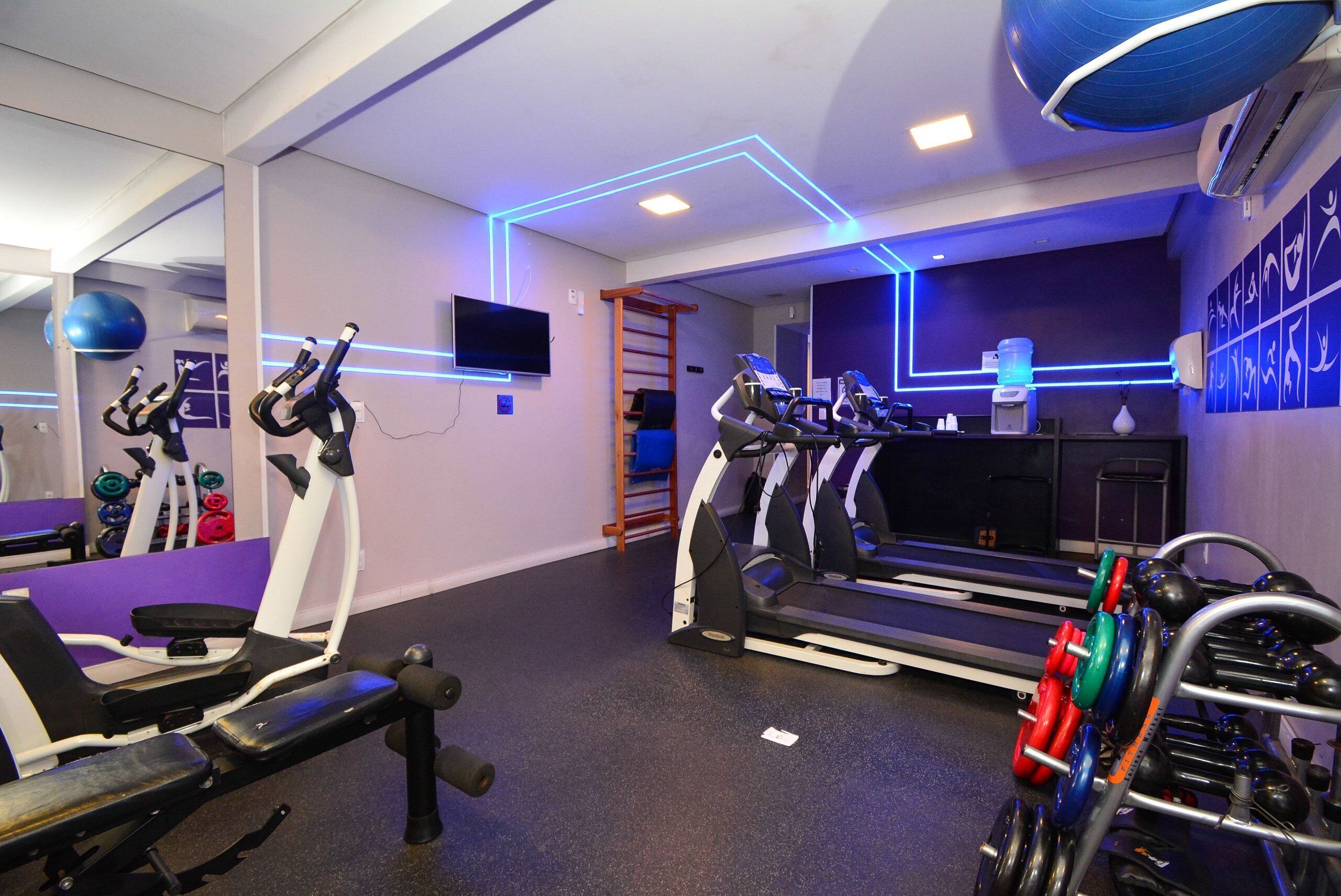 A gym with exercise equipment, a treadmill, and a wall-mounted TV.
