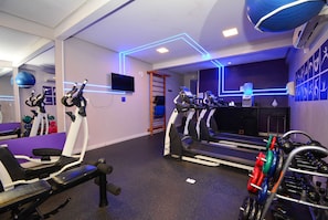 Una palestra con attrezzature per esercizi, tapis roulant e televisore a parete.