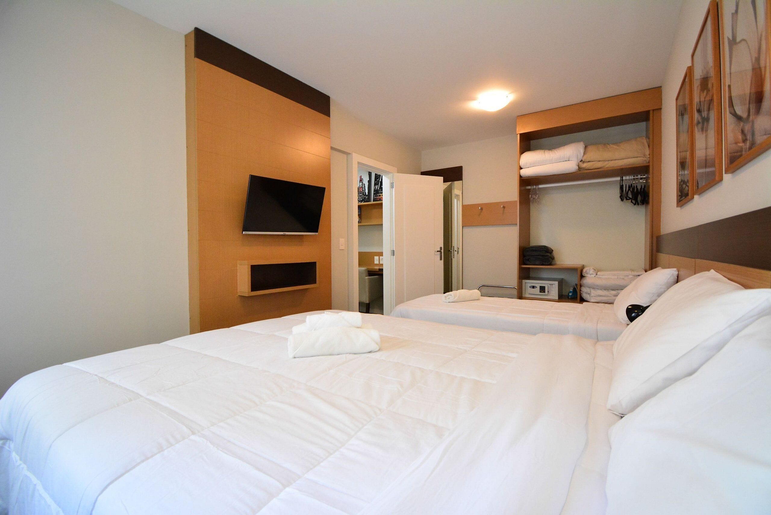 A hotel room with two beds, a TV mounted on the wall, and a walk-in closet with shelves and hanging clothes.