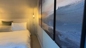 Una habitación de hotel con cama, almohadas y una obra de arte colgada en la pared.