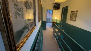 Un pasillo con paredes pintadas de verde, un banco de madera y obras de arte enmarcadas.