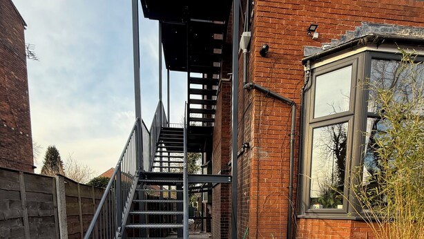 Una escalera conduce a un edificio con fachada de ladrillo y una ventana que ofrece vistas al cielo.