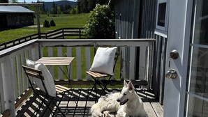 A wooden deck with a white dog, a table, and two chairs.