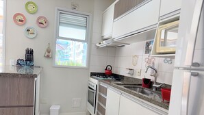 Une cuisine moderne avec des armoires blanches, une cuisinière à gaz, un four et un évier. Des assiettes décoratives ornent le mur, et une fenêtre offre une vue sur les bâtiments environnants.