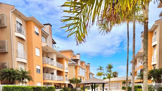 Une piscine avec des chaises longues, des palmiers et un immeuble à plusieurs étages doté de balcons.