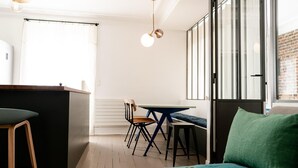 A modern room with a wooden floor, a green sofa, a dining table with chairs, and a kitchen area with a bar counter.