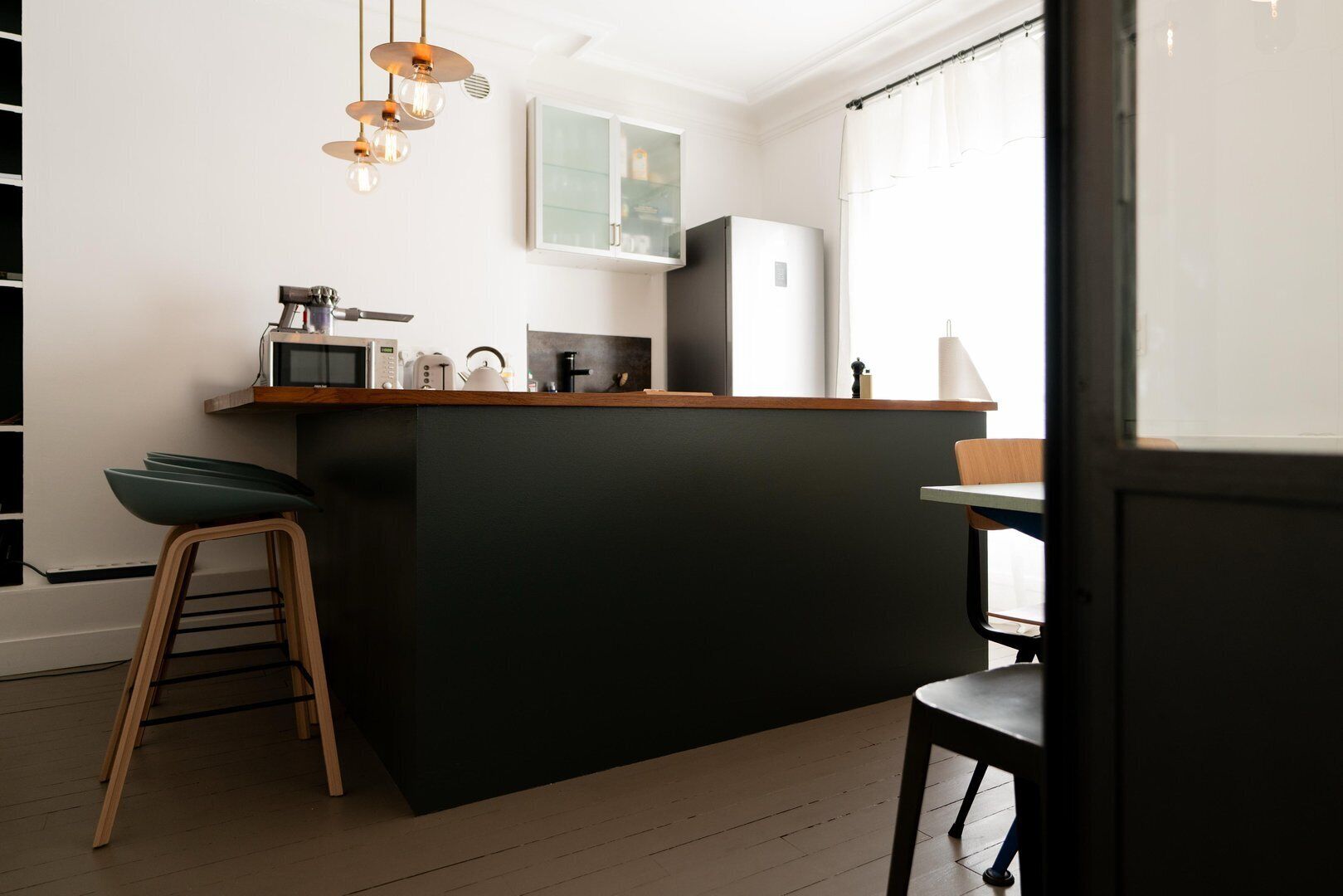 Una cocina moderna con una isla central, taburetes de bar, microondas, hervidor y refrigerador.
