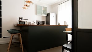 A modern kitchen with a central island, bar stools, a microwave, a kettle, and a refrigerator.