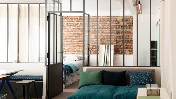 A modern bedroom with a brick wall, a bed with teal bedding, a desk, and a chair.