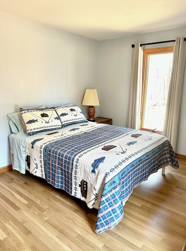 Un dormitorio con cama, mesita de noche, lámpara y ventana con cortinas.
