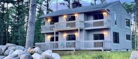 A multi-story wooden cabin with balconies, surrounded by a natural landscape with trees and rocks.