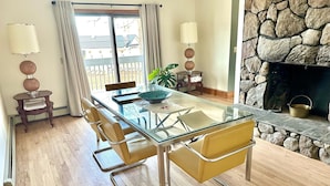 A dining area with a glass table, yellow chairs, and a stone fireplace.