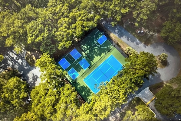An aerial view of a tennis court surrounded by dense greenery.