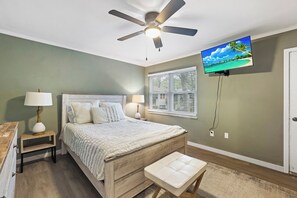 A bedroom with a bed, bedside tables, a ceiling fan, a TV, and a window.