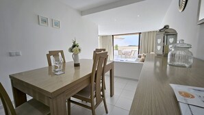 A modern dining area with a wooden table, chairs, and a vase with flowers. There is a view of an outdoor terrace with a table and chairs. - Albufeira Blue Wave Retreat 65 (Albufeira)