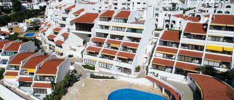 A high-rise hotel with multiple balconies, a central swimming pool, and a view of the surrounding buildings.