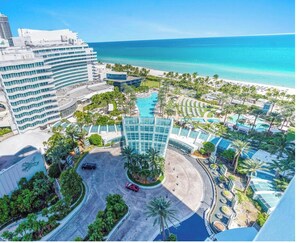 Ein Resort mit zentralem Pool, Palmen und Blick auf den Strand.
