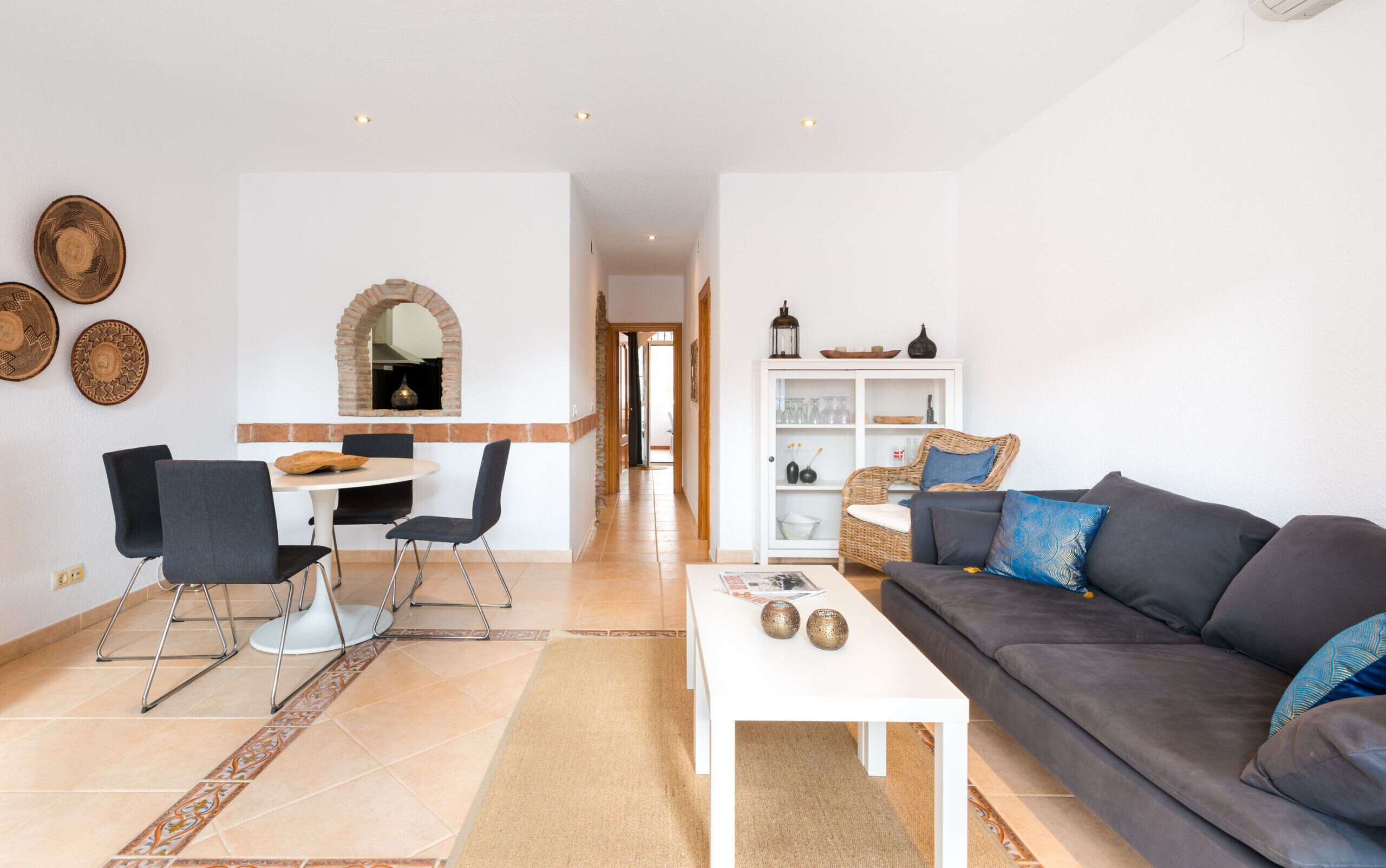 A modern living room with a grey sofa, a white coffee table, and a dining area with a white table and black chairs.