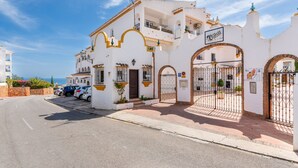Un edificio blanco con detalles amarillos, una entrada con reja y un letrero que dice 'Calle Real'.