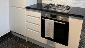 A modern kitchen with white cabinets, a black countertop, a stainless steel range hood, and a gas stove.